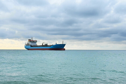 A large ship sails on the water in the ocean. The sky is filled with clouds, showing different shades of gray