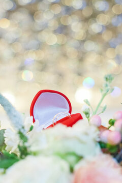 Engagement ring box surrounded by flowers in a soft focus background with lights during a celebration