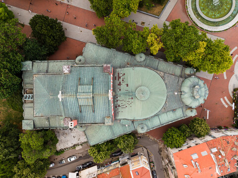 Aerial view of Opera Varna with its distinctive green copper roof and dome, surrounded by lush trees and a public square in Varna, Varna, Bulgaria.