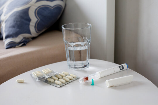 Medication drug, syringe pen and glass of water on a wooden nightstand at home