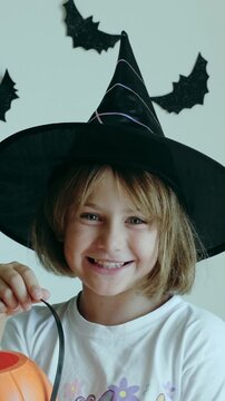 Video vertical portrait happy excited face girl trick or treat Halloween surprise kid wearing dress witch hat costume party Halloween. Toddler holding pumpkin jack lantern basket candies 