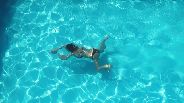 Female swimmer in a bright blue pool enjoying summer leisure and refreshing water. Recreation, health and summer vacation concept.