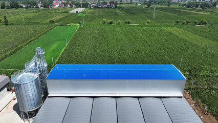 Aerial view of blue roof grain silo next to green farmland fields © zhu difeng