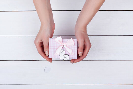 Girl gives a gift. Female hand holding a gift with a bow above the table.