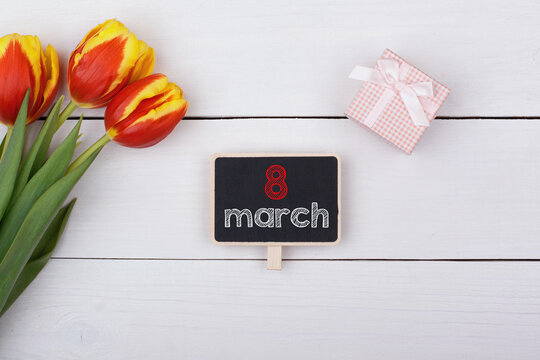 Blackboard with 8 March on the table, bouquet of tulips and a gift with a bow.