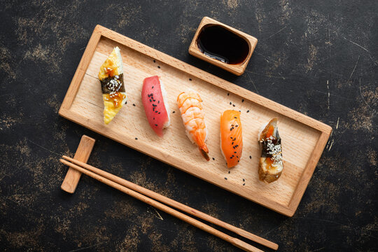 Set of Japanese sushi with soy sauce on a wooden plate with chopsticks, dark rustic background, top view, flat lay, copy space