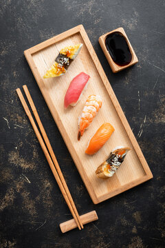 Set of Japanese sushi with soy sauce on a wooden plate with chopsticks, dark rustic background, top view, flat lay, copy space