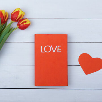 The red book Love on a white table. Flowers tulips and heart on the table.