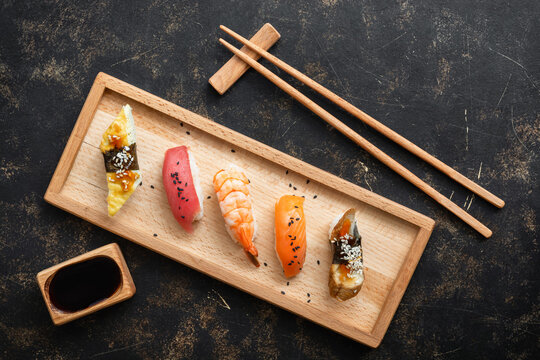 Set of Japanese sushi with soy sauce on a wooden plate with chopsticks, dark rustic background, top view, flat lay, copy space