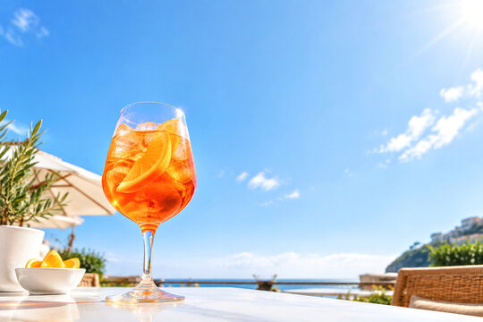 Orange spritz cocktail in stemmed glass with ice and orange slice on sunny outdoor table, refreshing summer drink