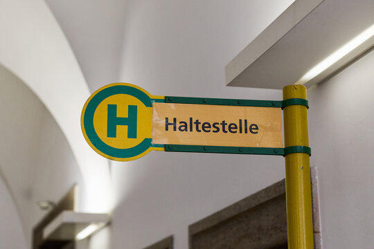 German bus stop sign with letter H and text Haltestelle on yellow and green pole indoors, close up.