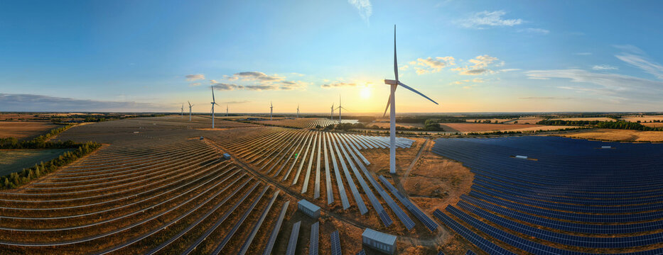 Aerial view of Chelveston Renewable Energy solar and wind farm with rows of solar panels and wind turbines under a golden hour sunset in Chelveston, England, United Kingdom.