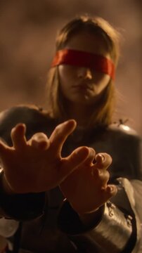 Vertical shot of blindfolded Caucasian young woman wearing medieval armor reaching hands forward. Footage suitable for historical drama trailers, fantasy game teasers, and cinematic promo campaigns