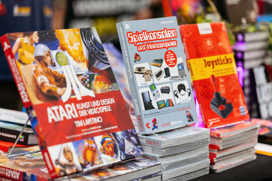 Cologne, Germany - August 26, 2026: Display of gaming books including Atari art and design, video game consoles, and joystick guides at a gaming trade fair