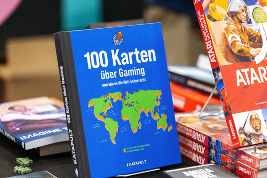 Cologne, Germany - August 26, 2026: Book titled "100 Karten uber Gaming" displayed on a table at a gaming trade fair with colorful covers of other books visible
