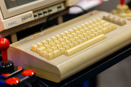Cologne, Germany - August 26, 2026: Vintage Commodore 64 keyboard displayed at a gaming trade fair with red joystick controllers visible in the background