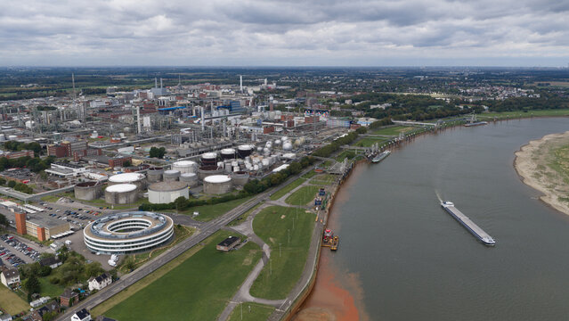 Aerial view of the Dormagen-Bayerwerk chemical plant with large storage tanks, industrial infrastructure, and a cargo barge on the Rhine river in Koln, Nordrhein-Westfalen, Germany.