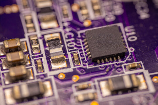 Close-up view of a printed circuit board featuring various electronic components including a microchip, resistors, and capacitors on a purple background