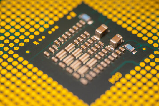 Close-up view of a computer microprocessor with gold pins and intricate circuitry on a green circuit board, showcasing advanced technology and engineering design