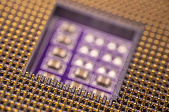 Close-up view of a microprocessor with gold pins and a purple substrate, showcasing intricate circuit patterns and electronic components in a detailed arrangement