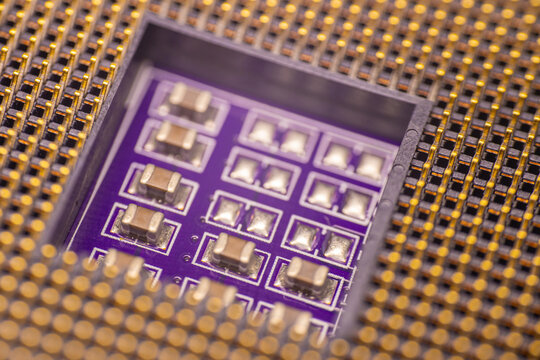Close-up view of a microchip with multiple electronic components on a purple circuit board, surrounded by a grid of gold-plated pins for connectivity
