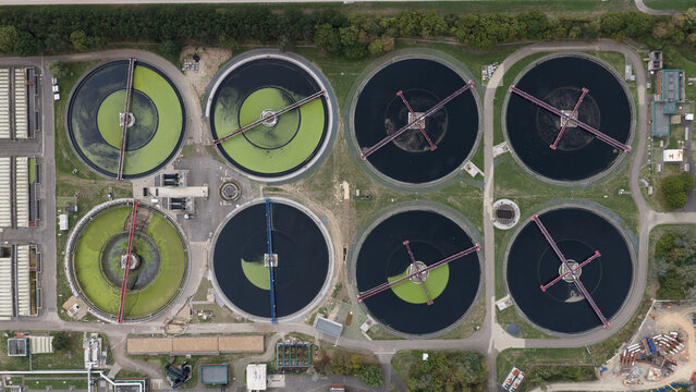 Aerial view of a wastewater treatment plant with circular sedimentation tanks, some containing green algae, Cologne, North Rhine-Westphalia, Germany.