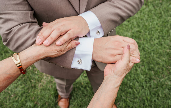 Manos de adulto mayor y hombre con traje mostrando afecto y apoyo familiar al aire libre