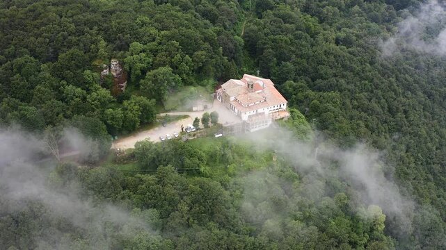 Aerial view of Mare de deu de la salut Hermitage, dramatically perched on a rocky cliff above dense forests, overlooking the beautiful mountain landscapes of Girona, Catalonia. 