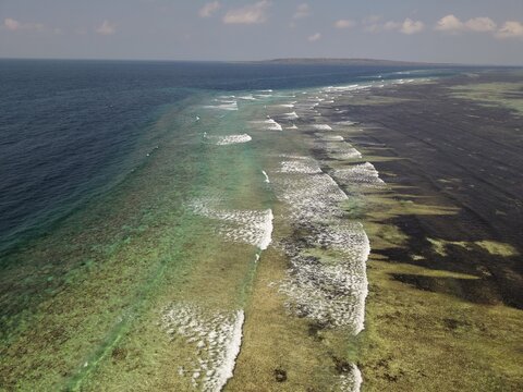 Aerial view of the coral reef and turquoise waters off the coast, showing the contrast between the shallow reef flats and the deep blue ocean in Tomia Timur, South East Sulawesi, Indonesia.