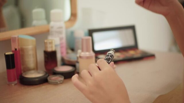 Woman applying makeup with brush at vanity table with cosmetics
