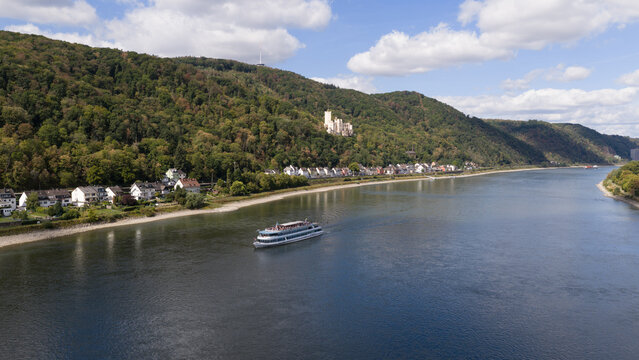 Aerial view of Stolzenfels Castle on a forested hillside overlooking the Rhine River with a cruise ship sailing past in Koblenz, Rheinland-Pfalz, Germany.