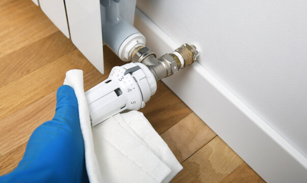 Hand in glove cleaning radiator thermostatic valve with a white cloth.
