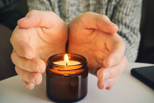 Hands cupping burning candle, symbolizing warmth, relaxation, and cozy atmosphere