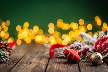 Naklejka premium A Christmas background featuring a red plaid bauble with a snowflake and gold ribbon, red ornaments, and frosted berries on rustic wood, set against green with twinkling lights and copy space.