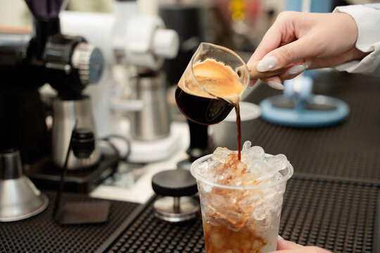 Iced coffee preparation concept with a barista pouring fresh espresso over ice in a clear cup at a cafe counter, representing coffee, espresso, iced, beverage, barista, refreshing, brewing.