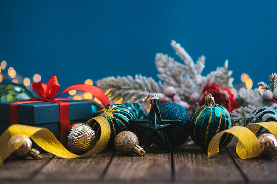 A Christmas background featuring navy and teal ornaments wrapped with gold ribbon on rustic wood, framed symmetrically against a deep blue backdrop with twinkling lights and copy space.