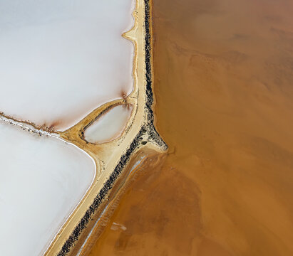 Aerial view of a salt lake with a striking contrast between white salt deposits and mineral-rich brown water, divided by a narrow sandy causeway in Australia.
