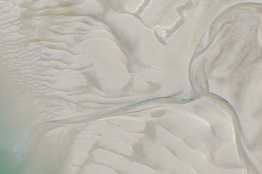 Aerial view of intricate sand patterns and tidal channels formed by receding water on a coastal beach in Australia.