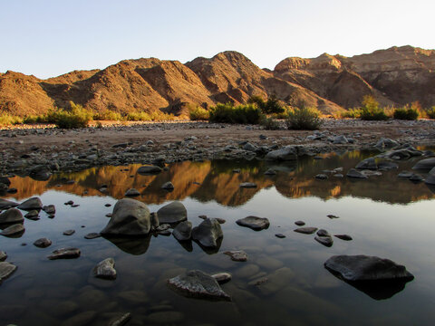 Tranquil scene of mountains reflecting into the Fish River, as seen from the base of the Canyon in Namibia. 
