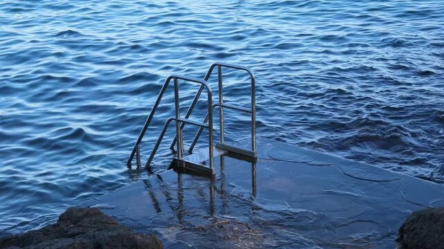 A video of a metal swimming ladder extending from a rocky bathing platform into the deep blue Adriatic Sea
