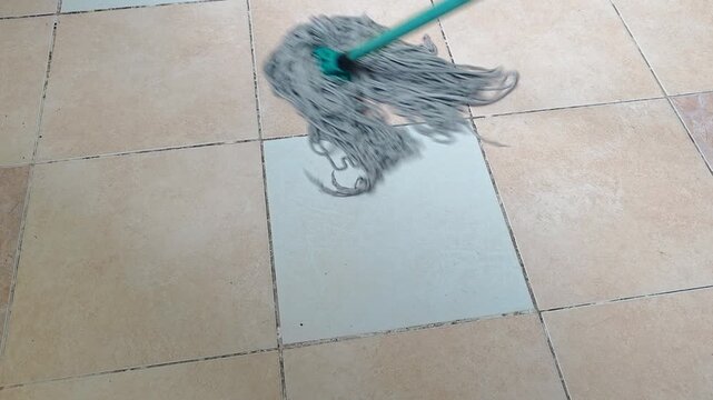 String mop cleans across tiled flooring in a wiping motion, floor cleaning routine, household maintenance scene.