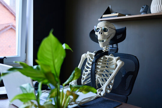 Skeleton wearing glasses and tie sitting at computer desk in home office