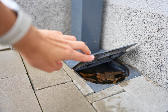 Person opens outdoor drain cover with leaves and debris inside