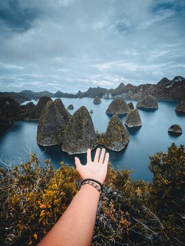 View of the limestone karst islands of Raja Ampat rising from turquoise waters under a cloudy sky in Indonesia.
