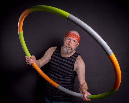portrait of senior man (in late 60s) exercising with a weighted hula hoop, fitness over 60 concept