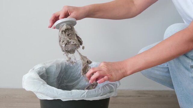 The woman is cleaning the vacuum cleaner filter of debris and dust.