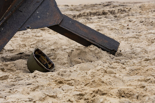 An American infantry helmet from World War II lies on the beach next to a czech hedgehog 