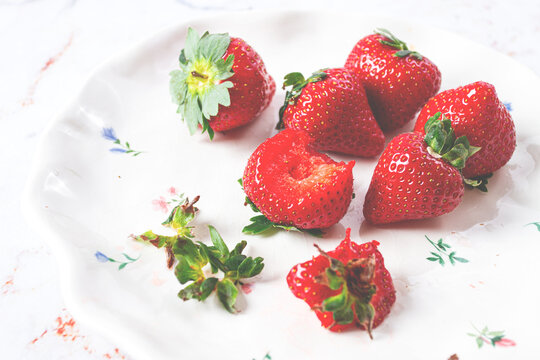 Fresh strawberries on a white plate with floral design arranged on a table