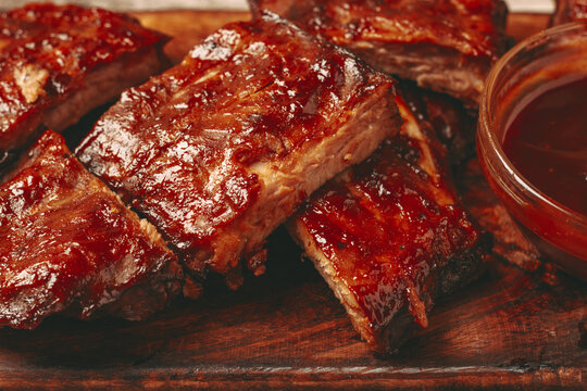 BBQ ribs with sauce served on a wooden board in a kitchen setting