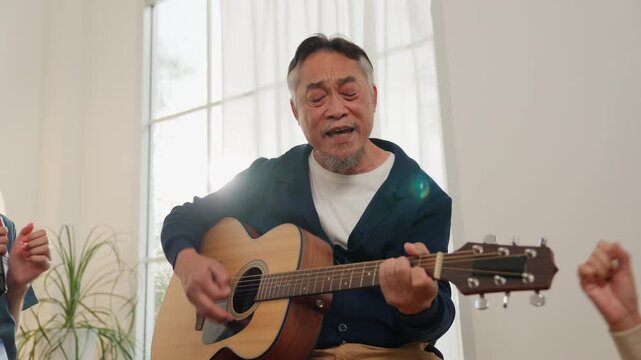 Senior man singing and playing acoustic guitar in bright room with music group during joyful retirement lifestyle elderly gathering warm light home leisure time